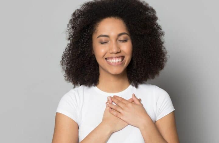 woman against a neutral background smiles and closes her eyes with her hands over her heart in gratitude