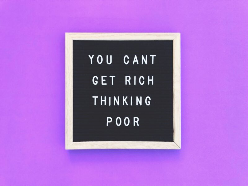Letter board against a purple background with text that reads You Cant't Get Rich Thinking Poor