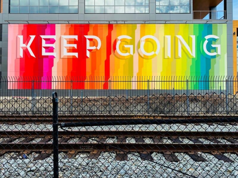 The words Keep Going on a wall in the city against a colorful rainbow background. A word of the month could be a phrase of the month too