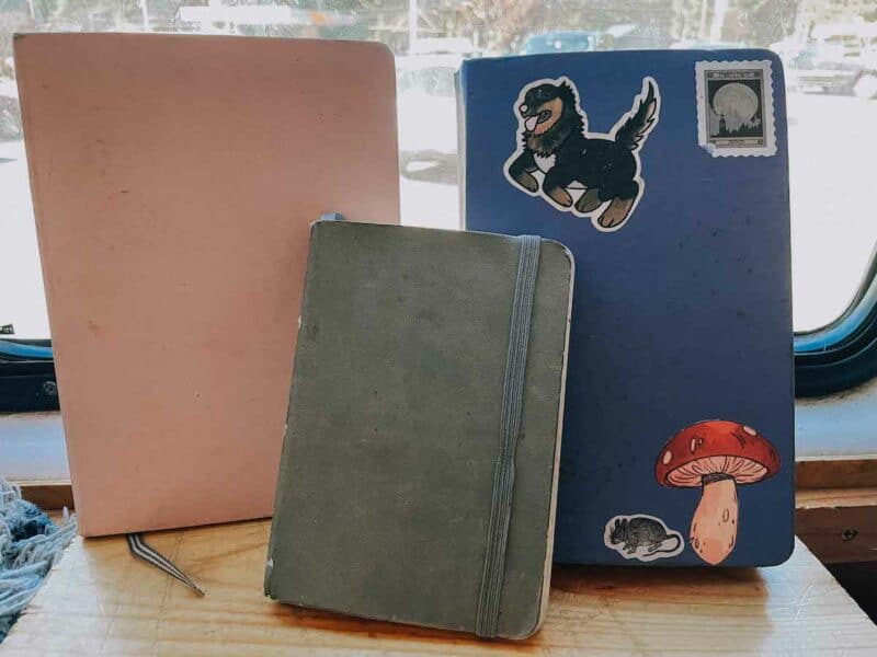 3 notebooks sit in the windshield of a van, filled with different creative notebook ideas for blank notebooks