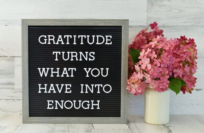 Letterboard sign that says "Gratitude Turns What You Have into Enough" next to beautiful vase of flowers