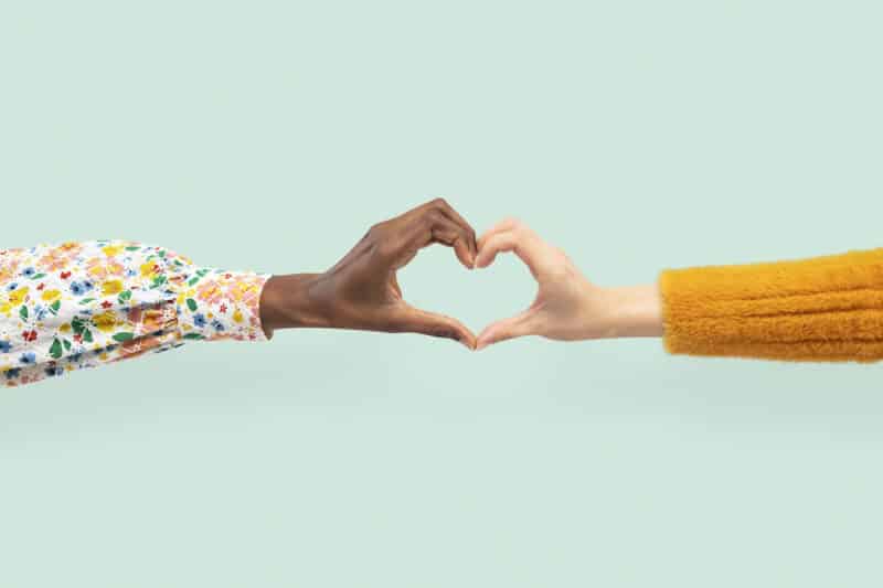 Two hands reaching together against a blue background to make a heart shape