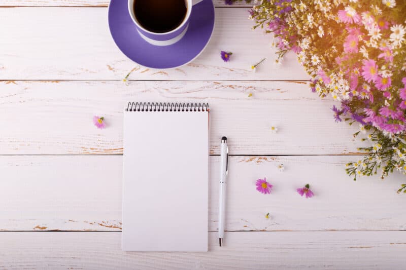 Morning journal with blank page, with pen, cup of coffee and bouquet of colorful aster flowers on white vintage background