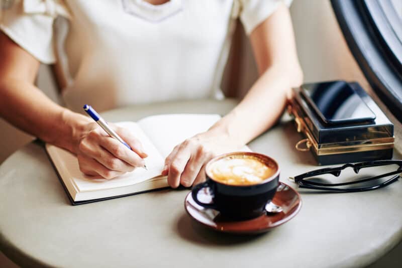 Woman writing in her morning journal with a cup of coffee on the table too