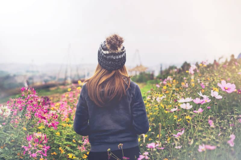 Make time in your Bullet Journal for self-discovery and unlock your potential. Young woman traveler walking in the flower field on the mountain